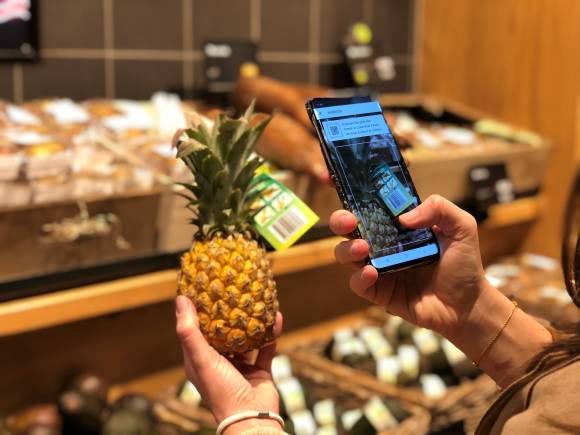 Frau scannt per Smartphone den Strichcode auf einer Ananas 