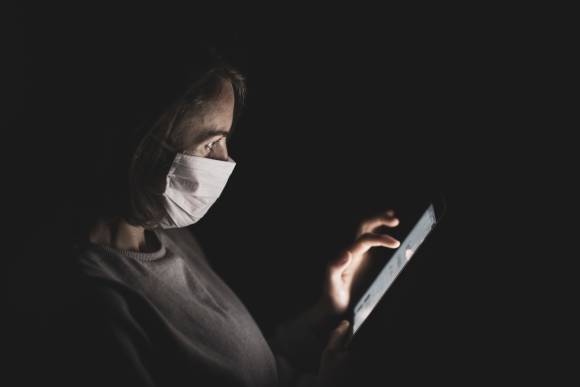 Frau mit Hygienemaske tippt auf Smartphone 