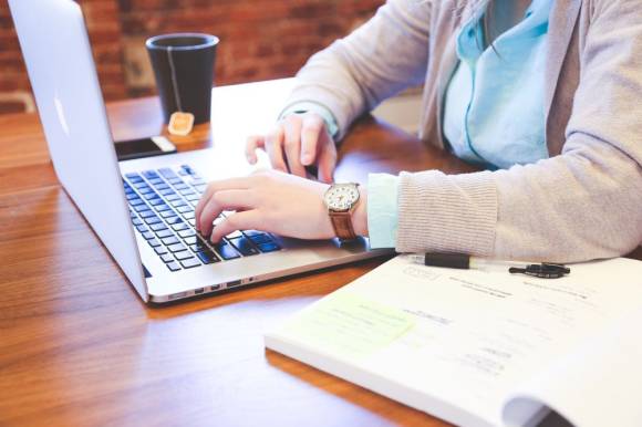 Person sitzt an einem Tisch und arbeitet auf einem Notebook 