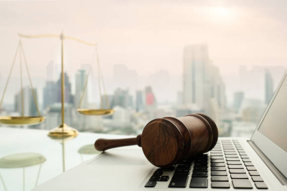 Waage und Gerichtshammer liegen auf Laptop-Tastatur, im Hintergrund Wolkenkratzer 