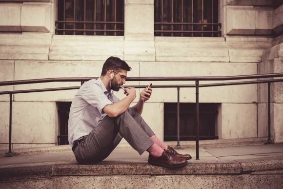 Mann sitzt auf Boden, hält Handy in Hand 