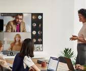 Eine Besprechung mit drei Personen in einem Sitzungszimmer sowie vier Personen via Teams-Bildschirm an der Wand