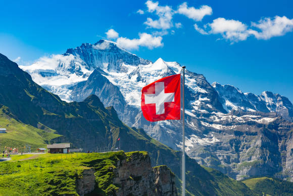 Symbolbild zeigt eine Alpenlandschaft mit wehender Schweizer Fahne 